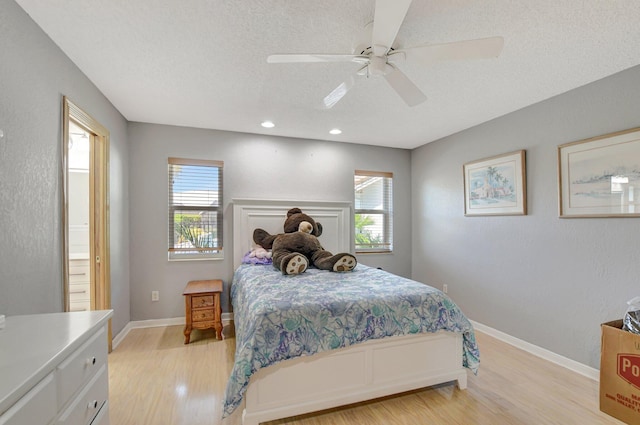 bedroom featuring ceiling fan, light hardwood / wood-style floors, multiple windows, and a textured ceiling