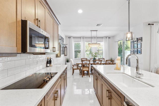 kitchen featuring sink, tasteful backsplash, light stone countertops, black electric cooktop, and decorative light fixtures