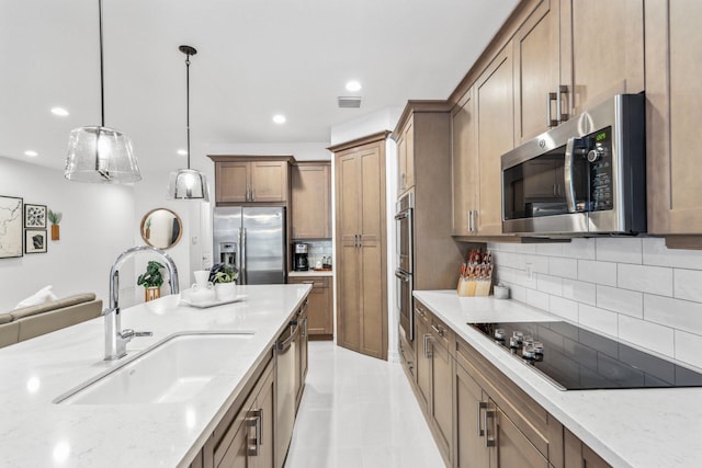 kitchen with light stone counters, appliances with stainless steel finishes, sink, and pendant lighting