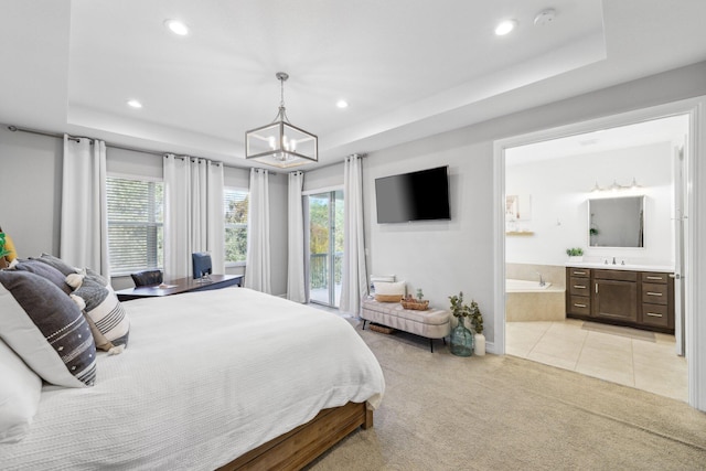 bedroom with light colored carpet, connected bathroom, a tray ceiling, and a notable chandelier