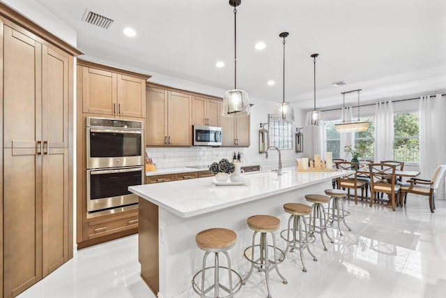 kitchen with a breakfast bar, pendant lighting, tasteful backsplash, an island with sink, and stainless steel appliances