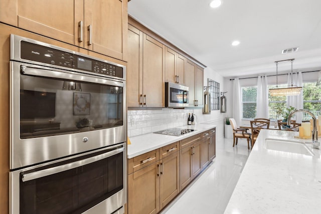 kitchen with pendant lighting, sink, decorative backsplash, light stone counters, and stainless steel appliances