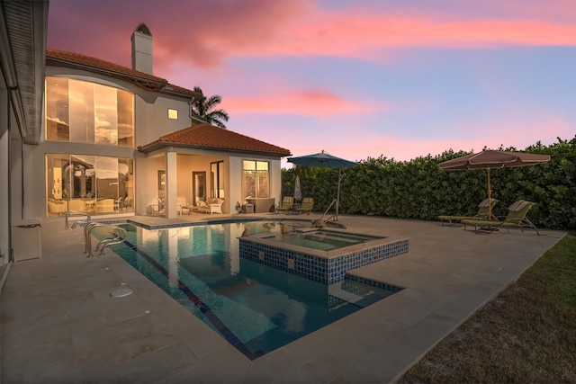 pool at dusk featuring an in ground hot tub and a patio area