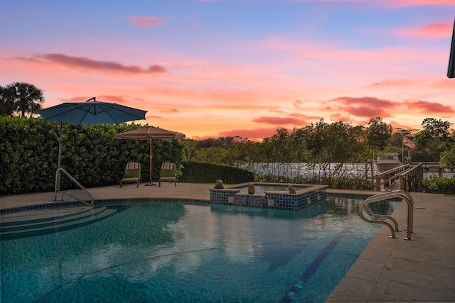 pool at dusk featuring a patio area and an in ground hot tub