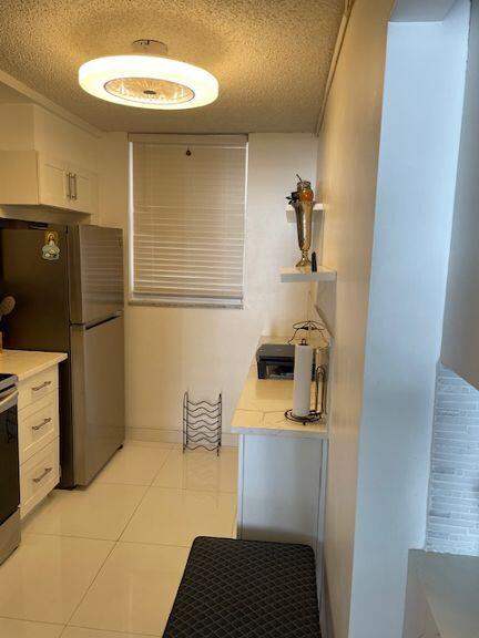 kitchen with stainless steel refrigerator, light tile patterned floors, a textured ceiling, and white cabinets