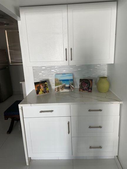 bar featuring tasteful backsplash, light stone countertops, and white cabinets