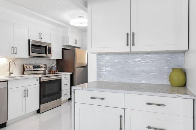 kitchen with sink, appliances with stainless steel finishes, light stone counters, tasteful backsplash, and white cabinets