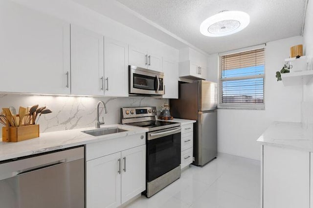 kitchen with white cabinetry, sink, light stone counters, stainless steel appliances, and a textured ceiling