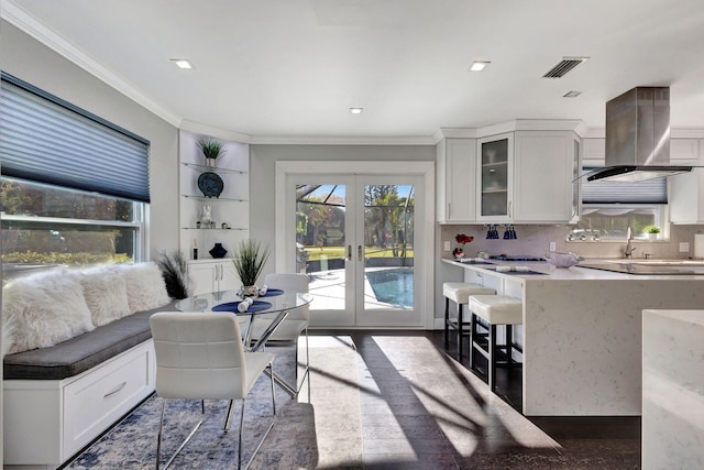 interior space with white cabinetry, backsplash, island range hood, ornamental molding, and french doors