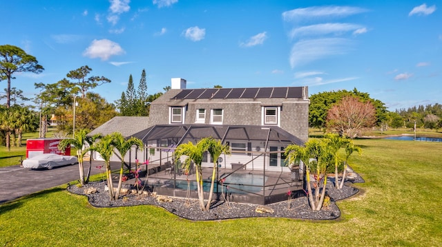 back of property with a lanai, a lawn, solar panels, and a water view