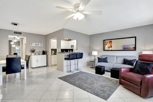 living room featuring ceiling fan, light tile patterned floors, and a textured ceiling