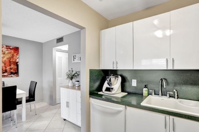 kitchen with white dishwasher, sink, light tile patterned floors, and white cabinets