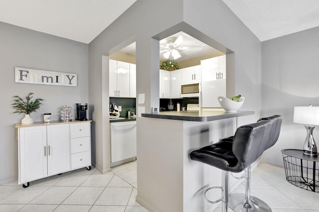 kitchen with light tile patterned flooring, white appliances, kitchen peninsula, and white cabinets