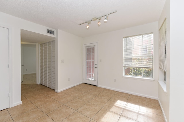 unfurnished room with rail lighting, a textured ceiling, and light tile patterned flooring