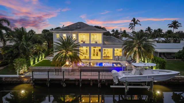 back house at dusk featuring a water view, a balcony, and a lawn