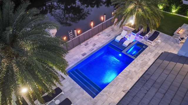 pool at night featuring an in ground hot tub and a patio area