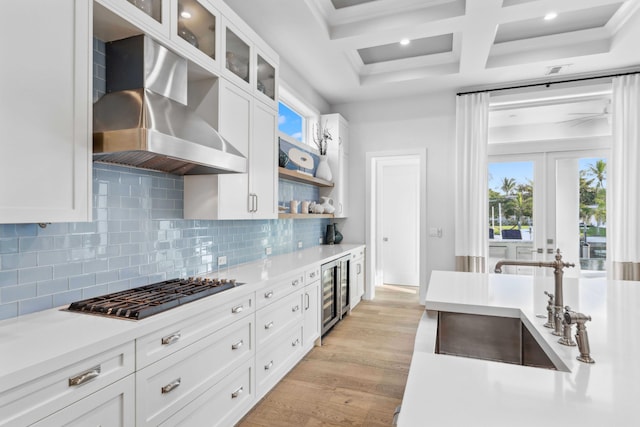 kitchen with wine cooler, white cabinets, stainless steel gas cooktop, and wall chimney range hood