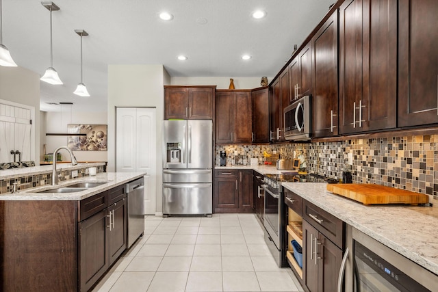 kitchen with pendant lighting, sink, stainless steel appliances, dark brown cabinetry, and light stone countertops