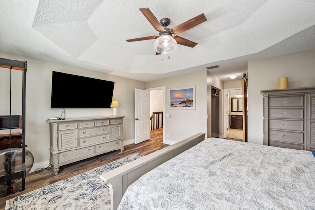 bedroom featuring connected bathroom, a tray ceiling, wood-type flooring, and a textured ceiling