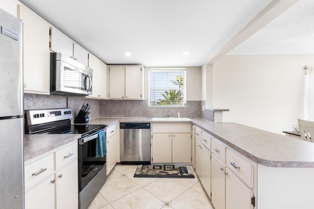 kitchen featuring appliances with stainless steel finishes, sink, backsplash, light tile patterned floors, and kitchen peninsula