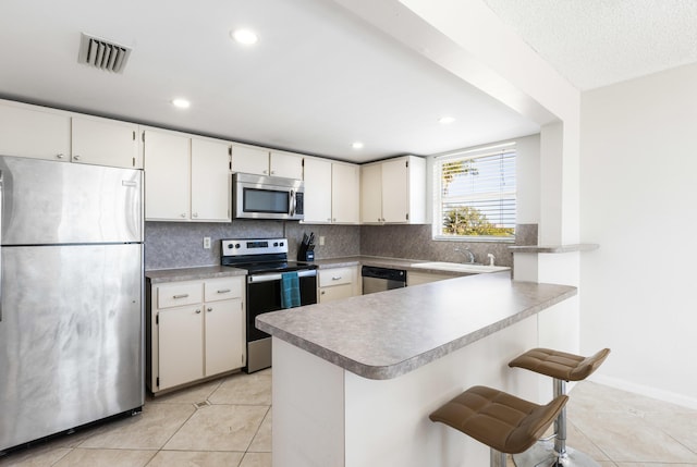 kitchen with appliances with stainless steel finishes, kitchen peninsula, decorative backsplash, and white cabinets