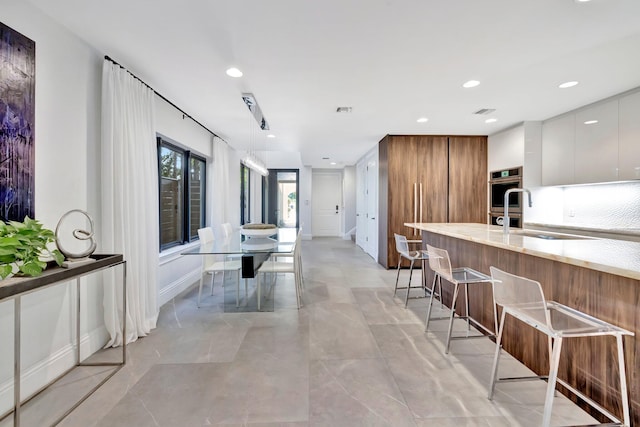 kitchen featuring a kitchen bar, decorative light fixtures, sink, and white cabinets