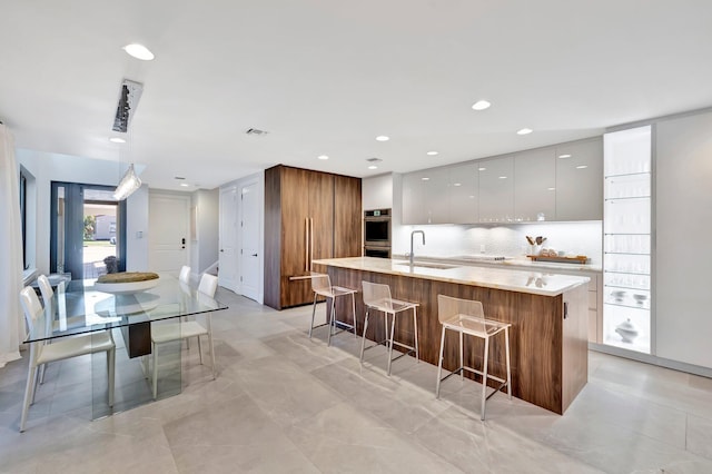 kitchen with white cabinetry, a kitchen bar, decorative backsplash, hanging light fixtures, and a kitchen island with sink