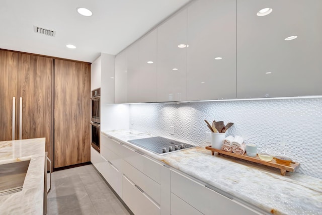 kitchen with black cooktop, backsplash, white cabinets, and light stone counters