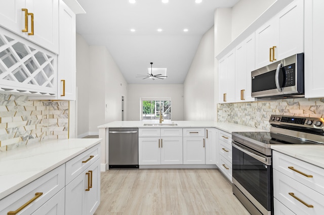 kitchen with vaulted ceiling, white cabinets, backsplash, light stone counters, and stainless steel appliances