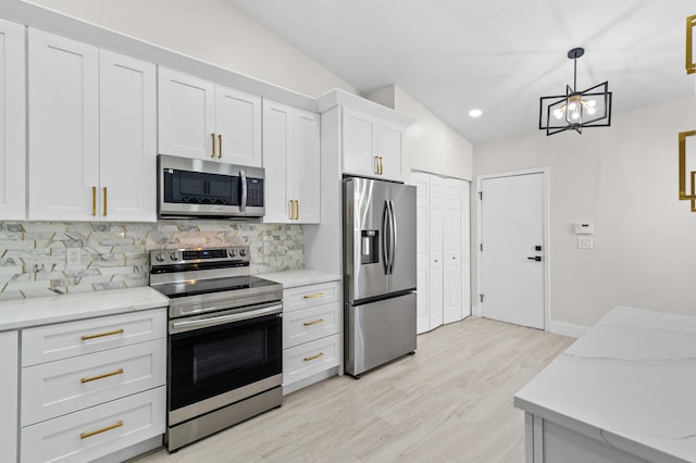 kitchen featuring vaulted ceiling, appliances with stainless steel finishes, white cabinetry, decorative backsplash, and hanging light fixtures