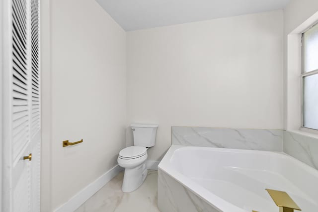 bathroom with plenty of natural light, tiled bath, and toilet