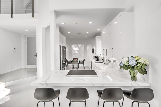 kitchen featuring a breakfast bar, sink, high end refrigerator, kitchen peninsula, and white cabinets