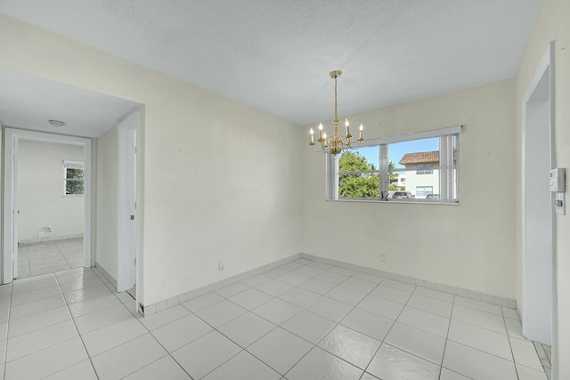 spare room featuring a notable chandelier, a textured ceiling, baseboards, and light tile patterned floors