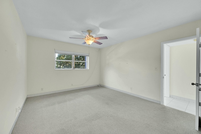 spare room featuring a ceiling fan, light carpet, and baseboards