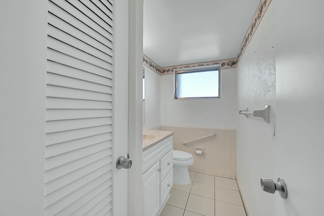 half bath featuring tile walls, a closet, toilet, vanity, and tile patterned floors