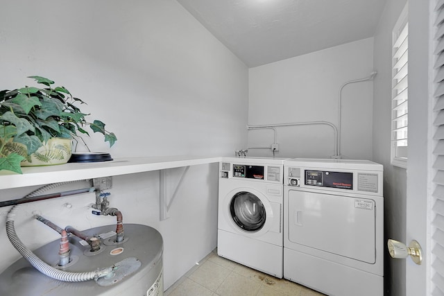 washroom featuring water heater, washing machine and dryer, and light tile patterned flooring