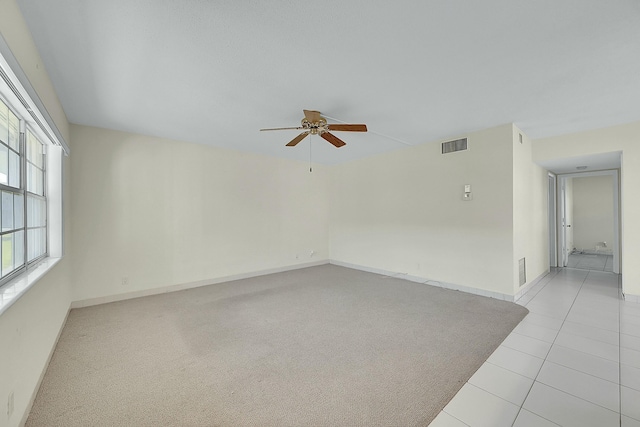 empty room with visible vents, a ceiling fan, light carpet, light tile patterned flooring, and baseboards