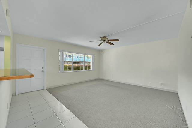 empty room featuring light carpet, ceiling fan, baseboards, and light tile patterned floors