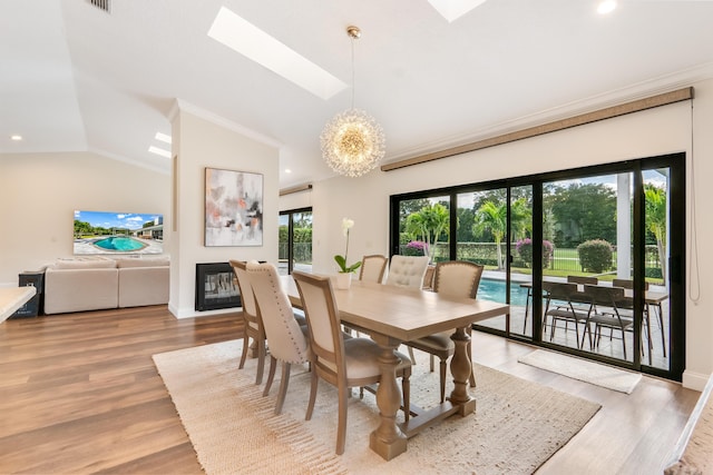 dining room with lofted ceiling with skylight, wood-type flooring, crown molding, and a chandelier