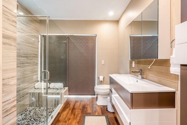 bathroom featuring hardwood / wood-style flooring, a shower with door, vanity, decorative backsplash, and toilet