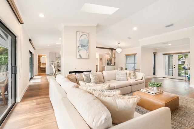 living room featuring lofted ceiling with skylight, crown molding, and light hardwood / wood-style flooring