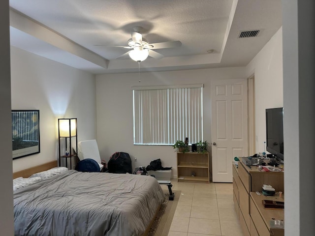 bedroom with light tile patterned floors, visible vents, a tray ceiling, and ceiling fan