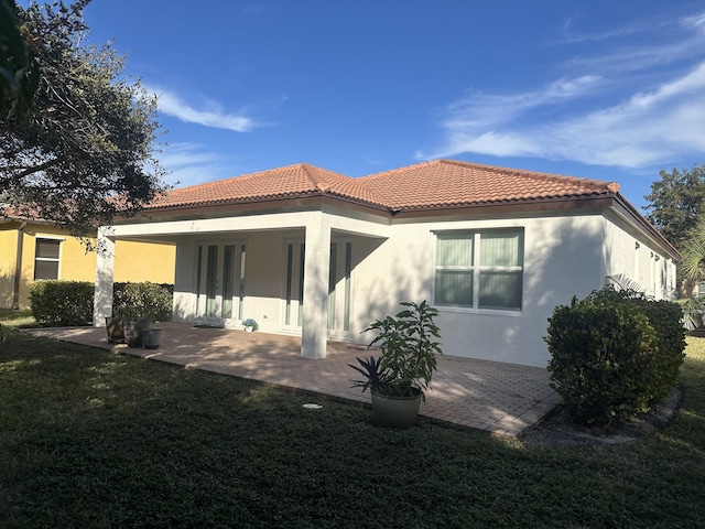 back of property featuring a tiled roof, a patio, a lawn, and stucco siding