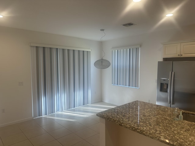 kitchen with stainless steel refrigerator with ice dispenser, visible vents, tile patterned flooring, white cabinetry, and dark stone counters