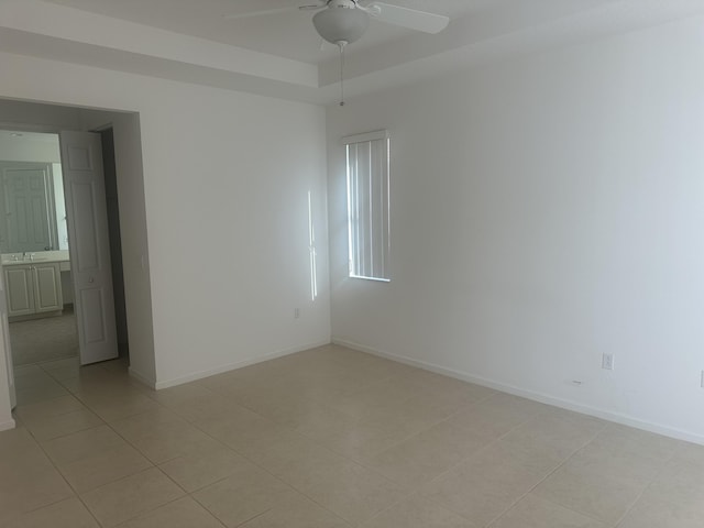 empty room featuring light tile patterned floors, baseboards, a raised ceiling, ceiling fan, and a sink