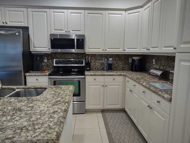 kitchen with light tile patterned floors, light stone counters, stainless steel appliances, white cabinetry, and backsplash