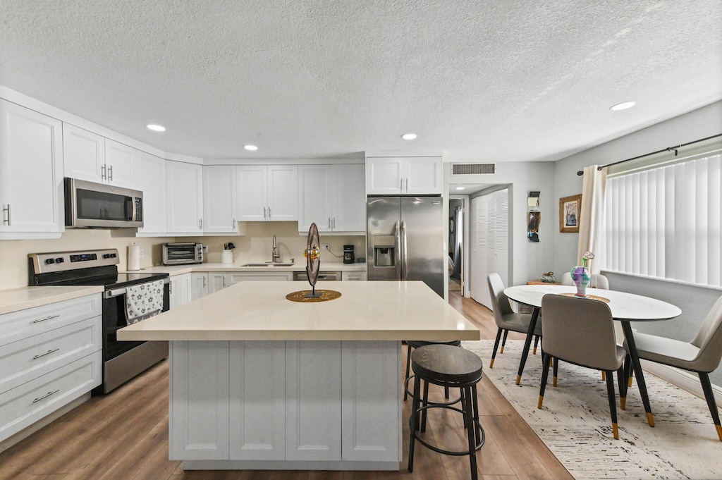 kitchen featuring sink, appliances with stainless steel finishes, hardwood / wood-style floors, white cabinets, and a kitchen island