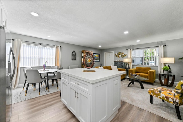 kitchen with stainless steel refrigerator with ice dispenser, white cabinetry, a center island, a textured ceiling, and light hardwood / wood-style floors