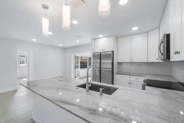 kitchen with pendant lighting, stainless steel appliances, a wealth of natural light, light stone countertops, and white cabinets