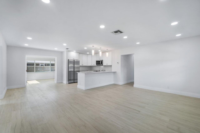 kitchen with appliances with stainless steel finishes, pendant lighting, white cabinets, kitchen peninsula, and light wood-type flooring